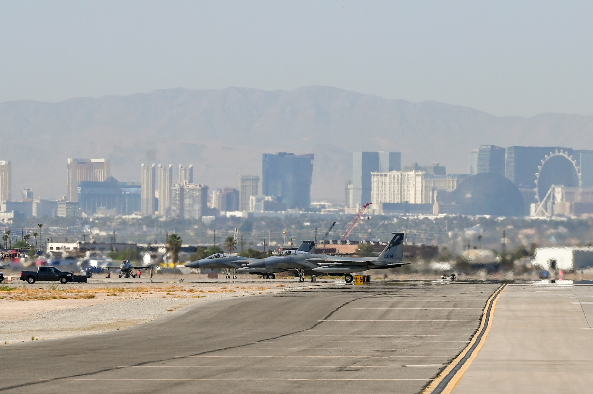 Two F-15C Eagles assigned to the 144th Fighter Wing park at the end of the runway, Sept. 13, 2024, in preparation for takeoff from Nellis Air Force Base with the Las Vegas skyline in the background