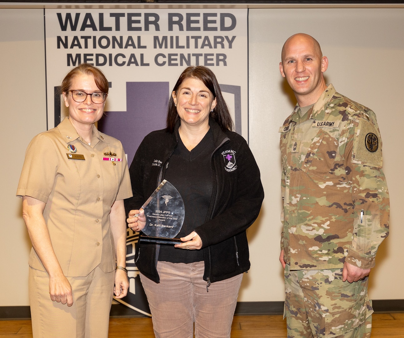 U.S. Navy CAPT (Dr.) Melissa Austin (left), director of Walter Reed National Military Medical Center and U.S. Army Master Sgt. Joshua Queen, WRNMMC senior enlisted leader, presents Dr. Kelli Bankard with the Army LaFleur Rx Educator Award during Walter Reed's town hall meeting on December 10.