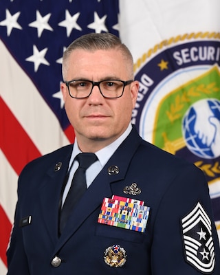 CMSgt Sundin poses in front of the American flag and the DSCA flag for his official portrait.