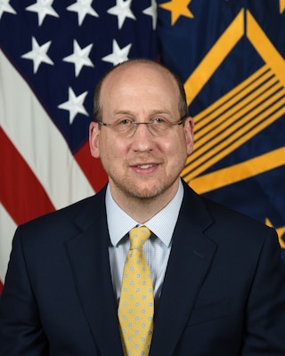 Mr. Robert Helfant stands in front of American flag and SES flag for his official portrait