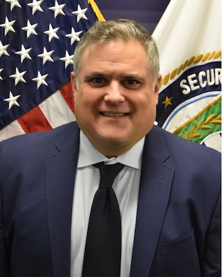 Mr. David Ferrari poses in front of the  American flag and the DSCA flag for his official portrait.
