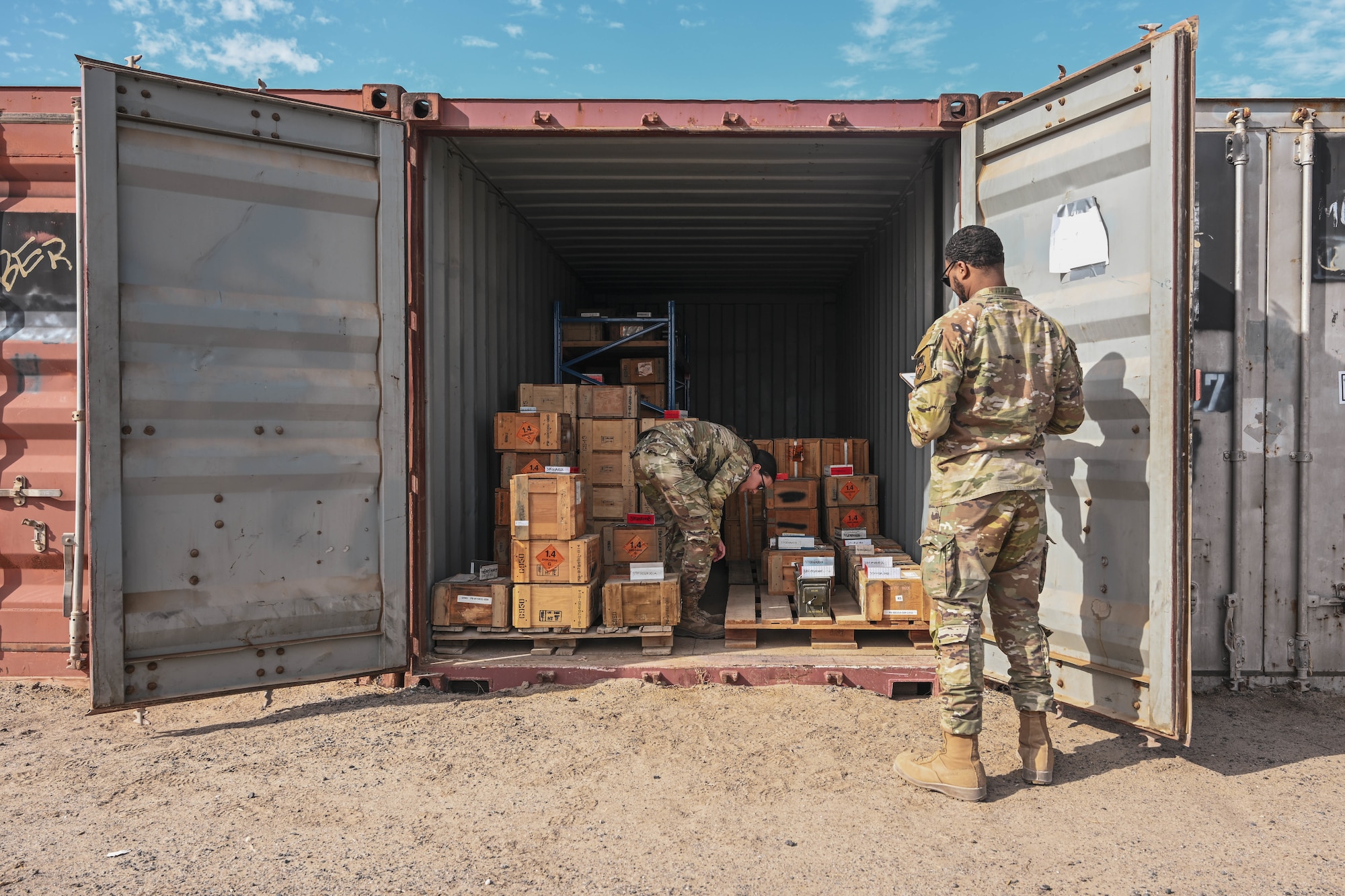 Two men in uniform conduct inventory in a shipping container.
