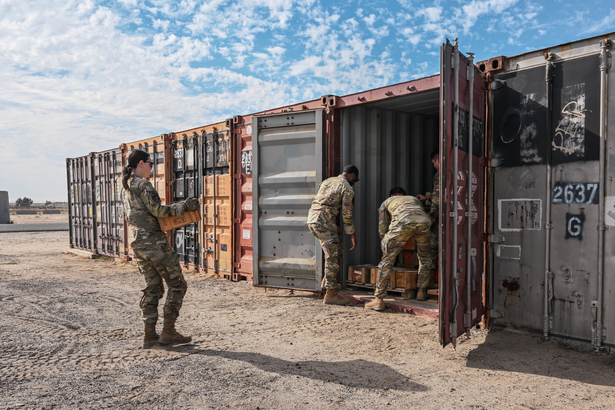 A group of people in uniform move boxes into a shipping container.