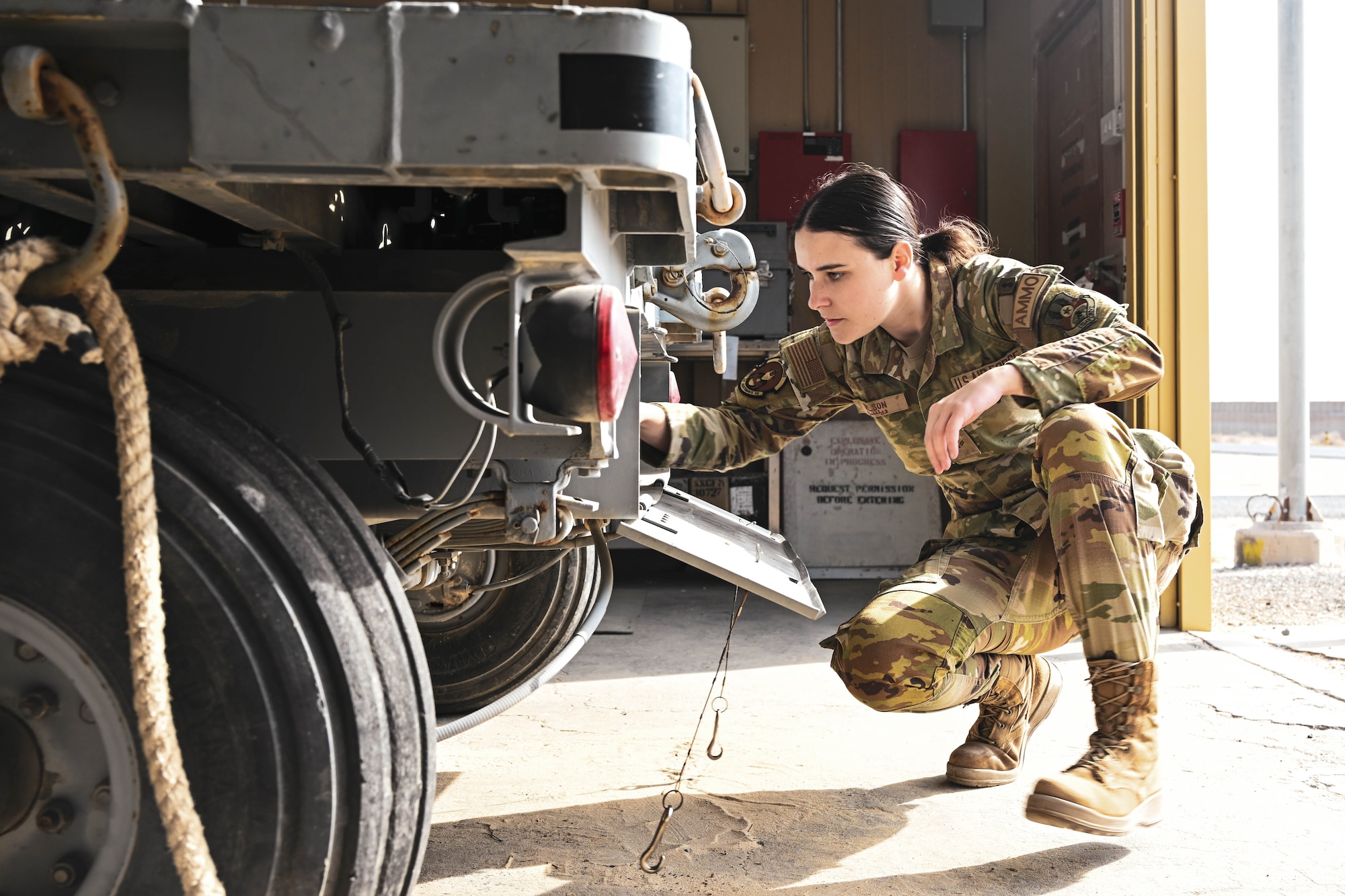 A woman in uniform kneels down and looks into a trailer.