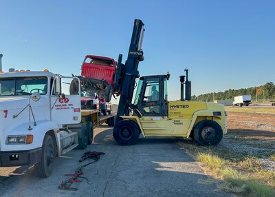 A large forklift removes a truck from a flat bed semitruck.