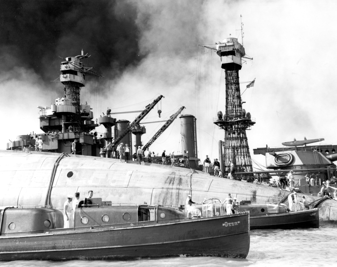 Three small ships float near the upturned hull of a larger ship.