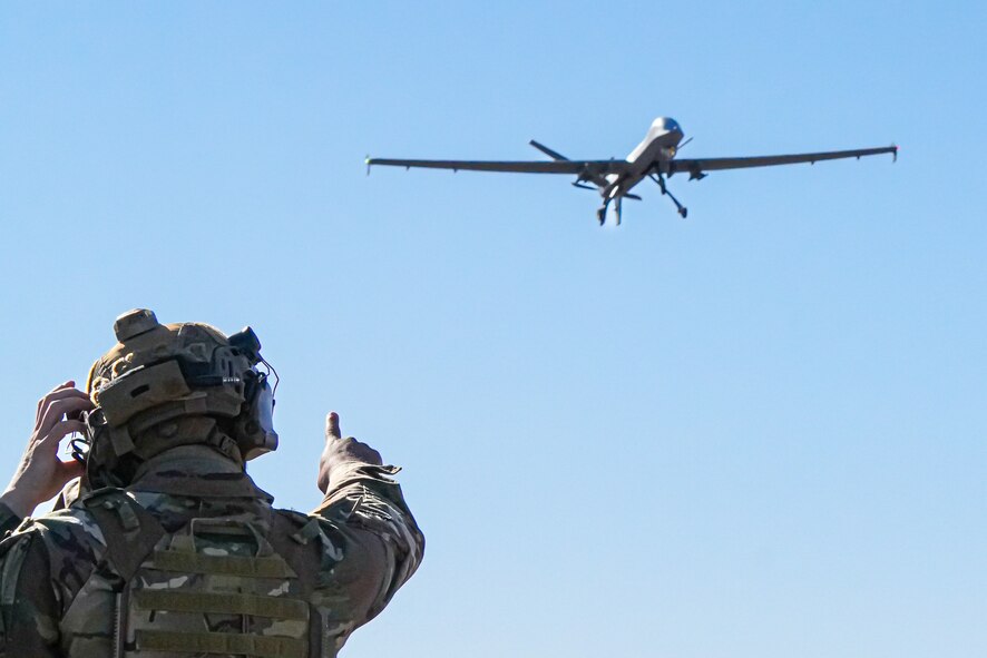 A U.S. Air Force Airman assigned to the 1st Special Operations Support Squadron Mission Sustainment Team watches as an MQ-9 Reaper prepares to land on an unprepared dirt surface