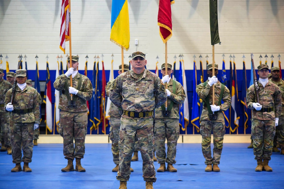 Soldiers holding flags stand in formation in a large room.