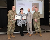 Photo of Paula Mesaris being presented and award by Depot Commander James L. Crocker, Deputy Commander Robert Lantka, and Depot Sgt. Maj. Michael S. Riggs.