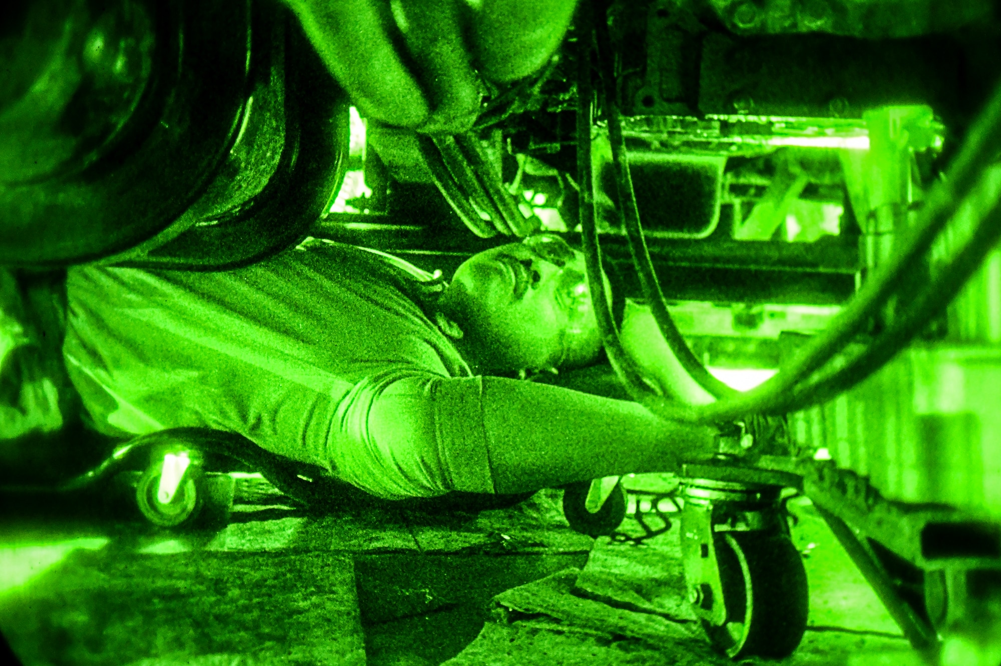 night vision shot of a mechanic working underneath a snowplow.