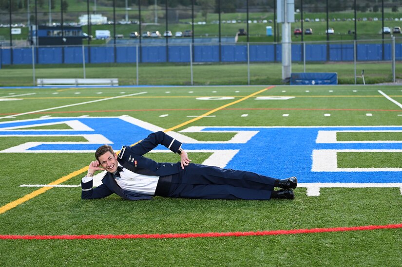 A smiling person in a military uniform poses lies on a sports field.