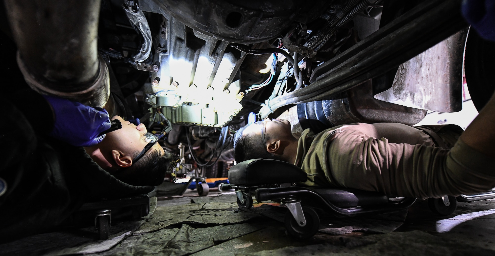2 military members fix a transmission under a snowplow.