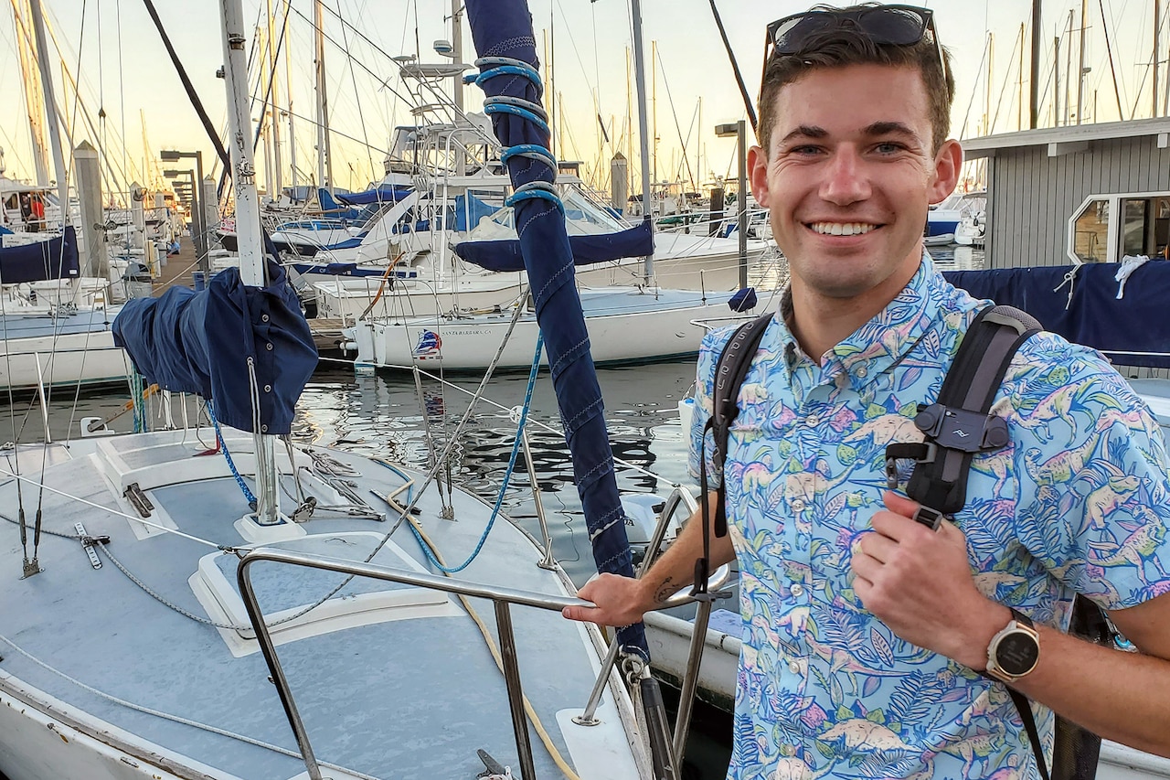 A smiling person poses for a photograph in front of boats at a pier.