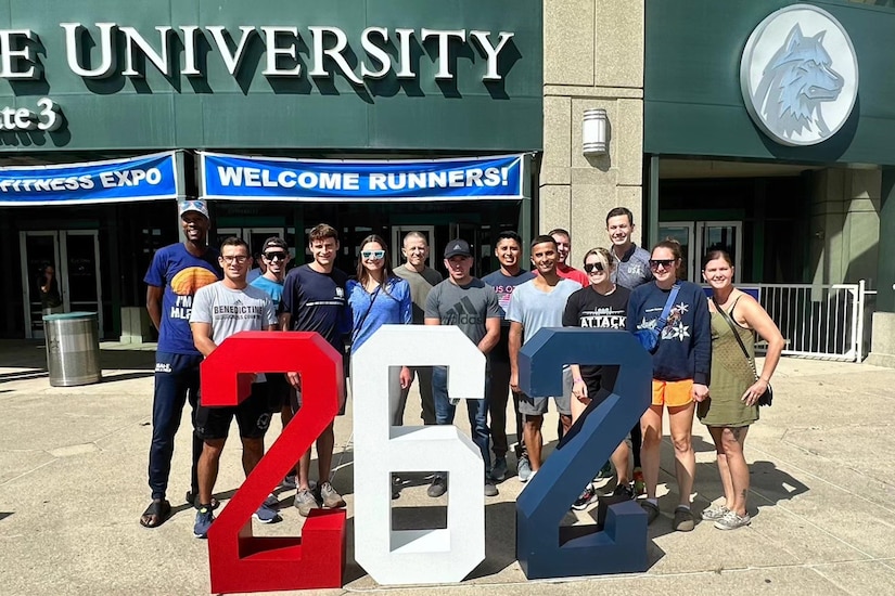 Two rows of people pose for a photo in front of a sports arena. Large decorative numbers reading "262" are in front of them.