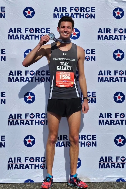 A smiling Air Force Marathon runner holds a medal while posing for a photo.