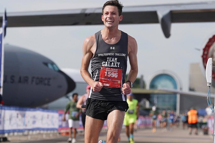 A smiling runner crosses the finish line of a marathon.