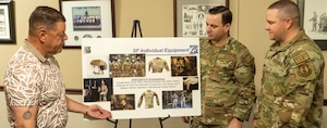 Shaeffer and two military members look at a board with pictures of female helmets, vests and holster systems.
