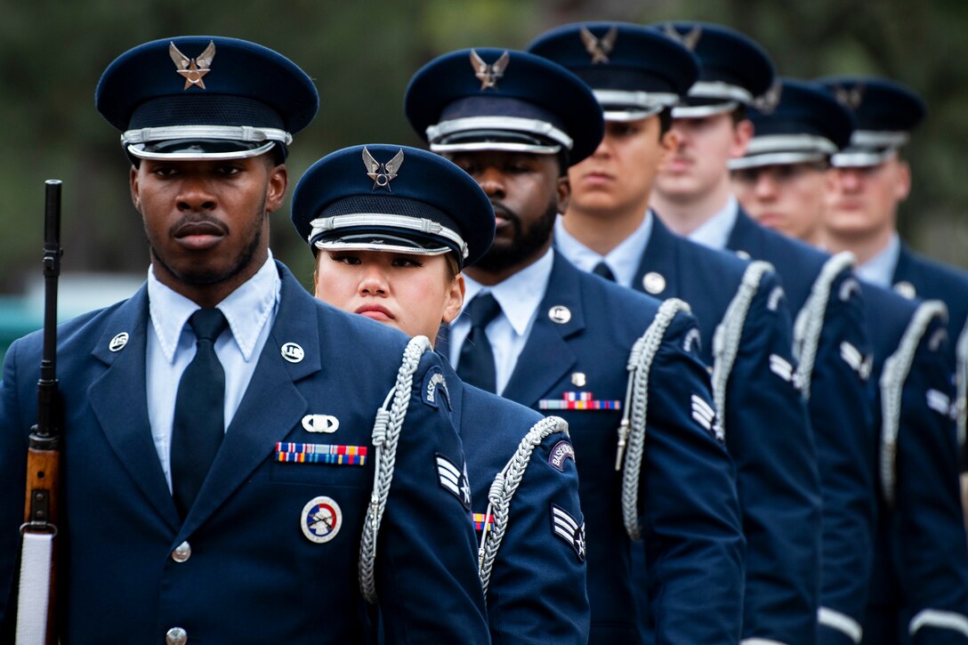 Seven airmen in dress uniforms stand in a line outdoors.