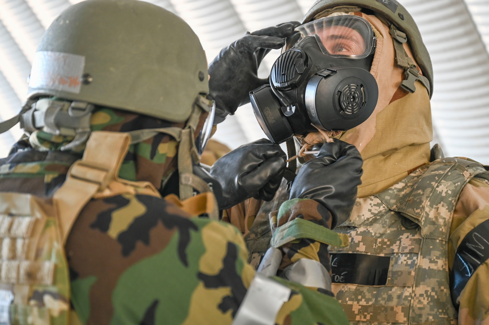 One Airman ties a string on the other Airman's MOPP gear