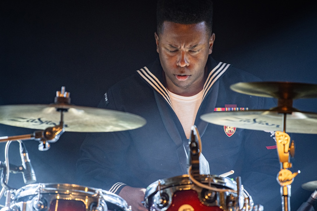 A uniformed service member plays the drums during a concert.