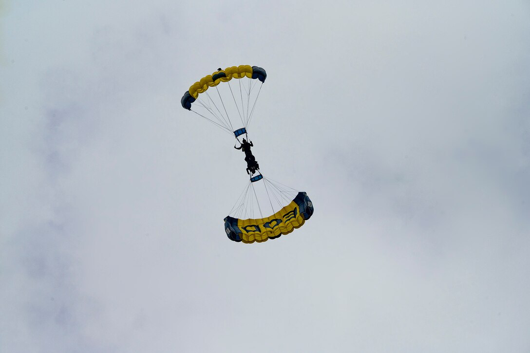 Two Navy parachute team members perform a tandem skydive against an overcast sky.