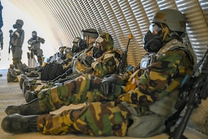 Airmen sit against a wall in MOPP gear