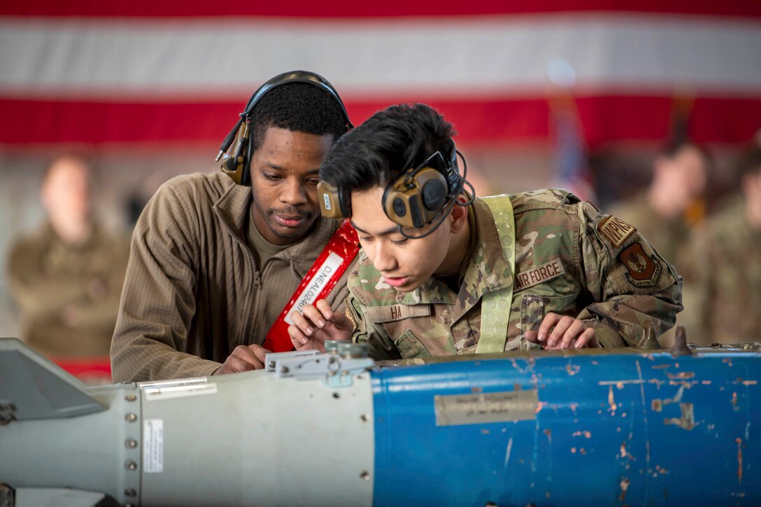 Two airmen wearing headsets stand next to each other while inspecting a weapon.