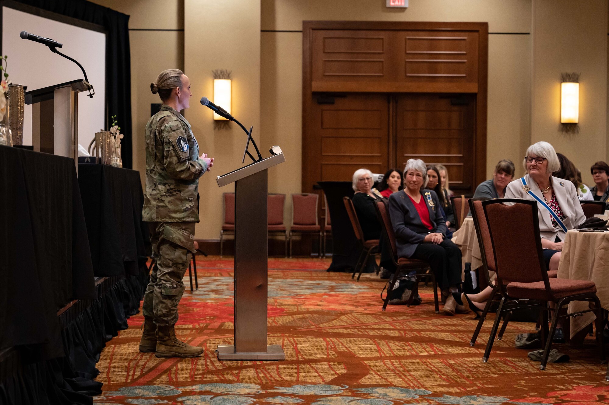 service member speaks at podium in front of crowd.