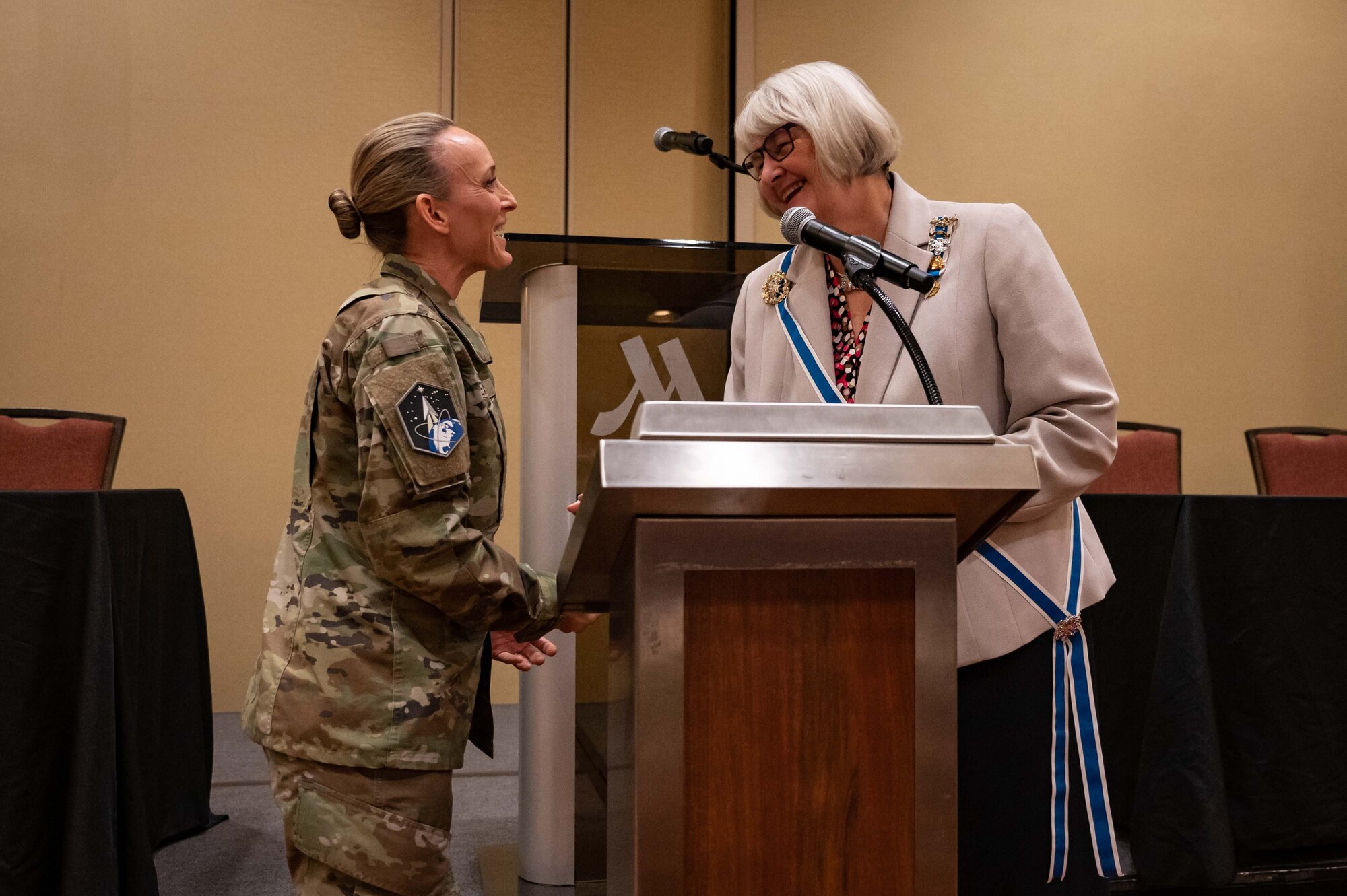 servicemember shakes hand with woman behind podium.