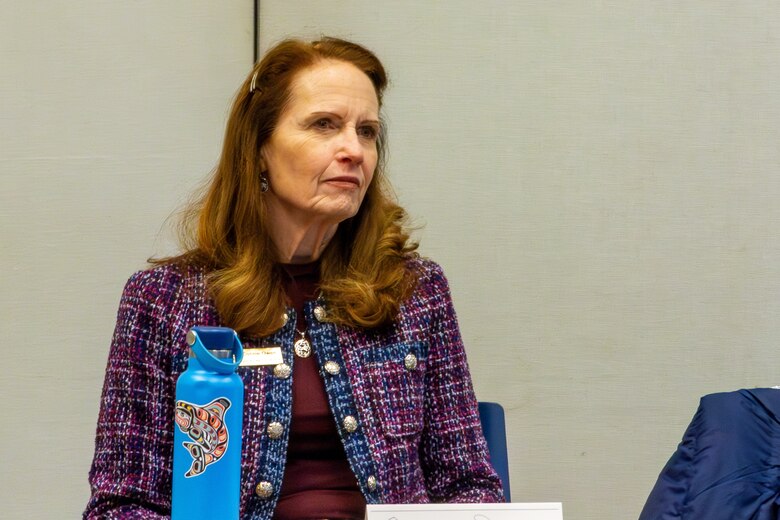 A woman in a purple plaid jacket looks to the right with a blue water bottle in front of her.
