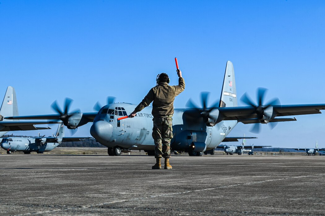 An Airman stands in front of a plane doing arm signals.