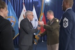 Assistant Secretary of Defense for Sustainment Christopher Lowman hands the DLA LTG Mark Simerly with VADM Michelle Skubic and CCM Alvin Dyer looking on