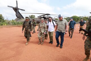 Military leaders walk as a helicopter sits in the background.