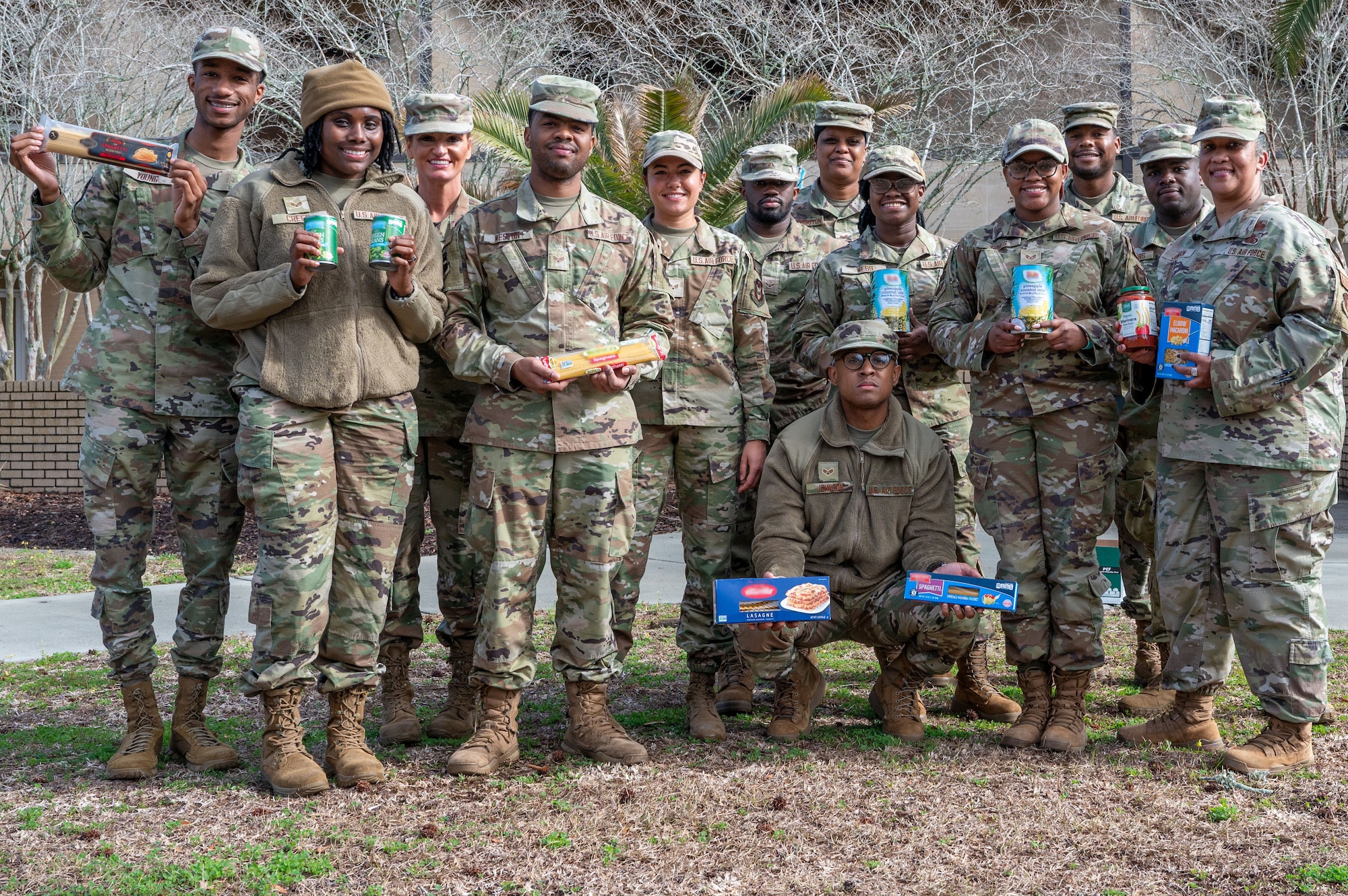 A group of Airmen display canned food and other items for a food drive