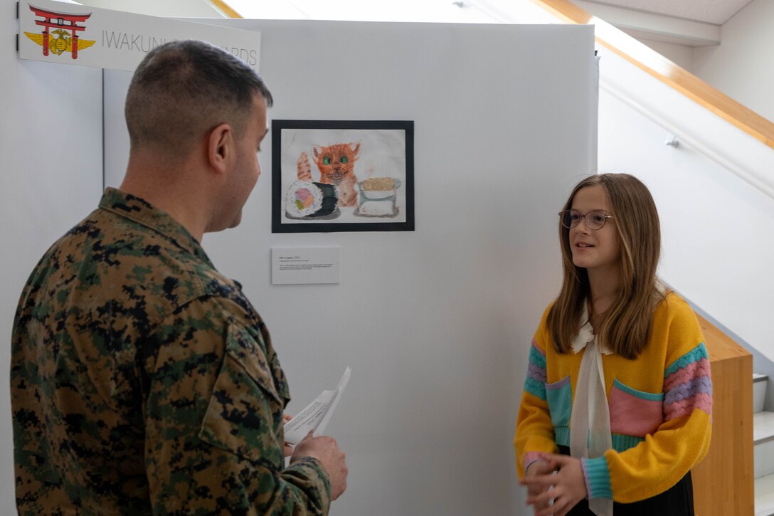 A student from Iwakuni Intermediate School, right, describes her artwork to U.S. Marine Corps Col. Richard Rusnok, the commanding officer of Marine Corps Air Station Iwakuni, during an art awards presentation at MCAS Iwakuni, Japan, Jan. 25, 2024. The air station presented awards for its monthly art competition in which students attending schools at the air station showcase their artistic talent through different art mediums. (U.S. Marine Corps photo by Lance Cpl. Colin Thibault)