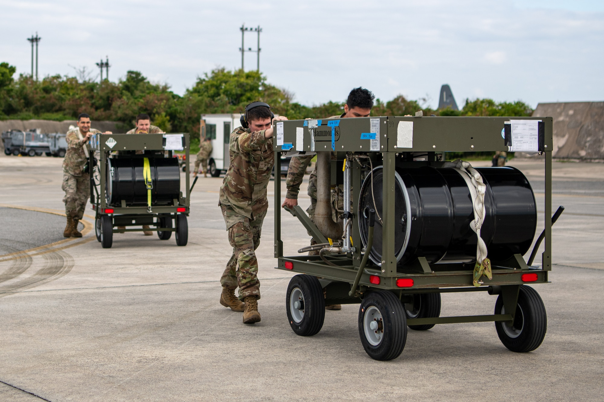 Four Airmen push carts on the Kadena flight line.
