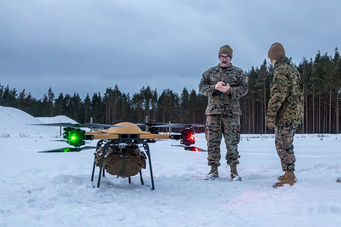 Two Marines talk while standing in a snowfield near a parked drone.