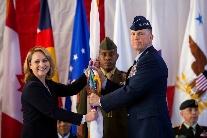 A civilian and a military officer hold a flag while another service member stands behind them.