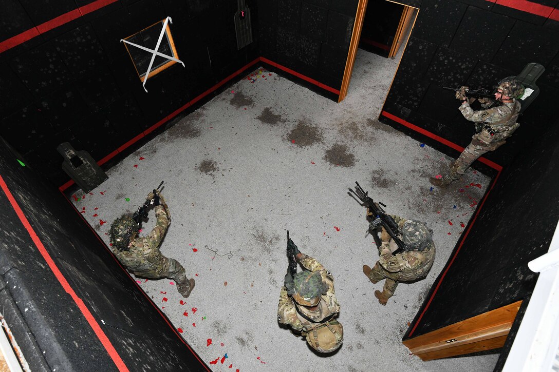 Four soldiers aim their weapons in an empty room as seen from above.