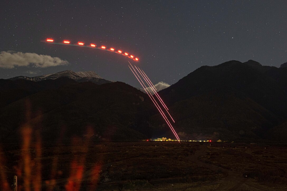 The lights of a helicopter are seen across a starry sky as other lights beam to the ground.