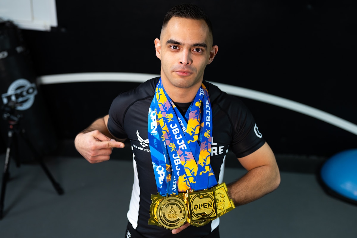 Man holds gold medals in Brazilian Jiu-Jitsu practice uniform.