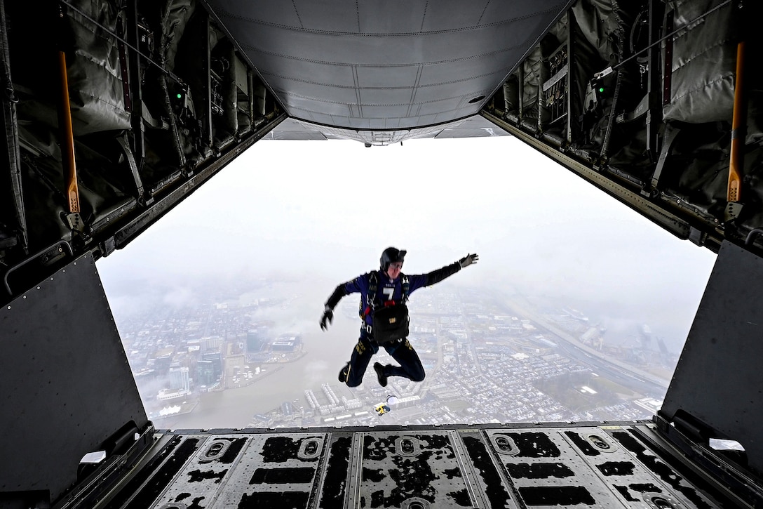 A service member wearing a parachute jumps from a military aircraft.