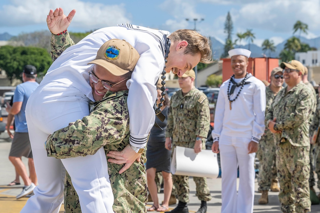 A Navy sailor lifts another sailor over his shoulders during a homecoming event.