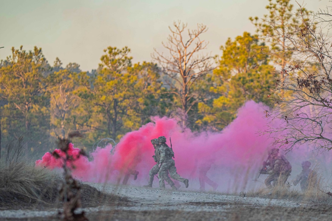 Soldiers run through a wooded area using pink smoke as a cover.