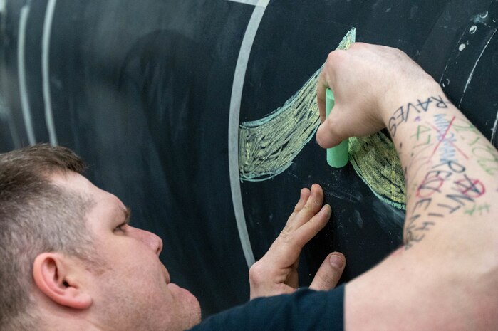 An Airman from the 99th Expeditionary Reconnaissance Squadron draws the first chevron of the Army rank for sergeant as part of a memorial drawing on a U-2 Dragon Lady.