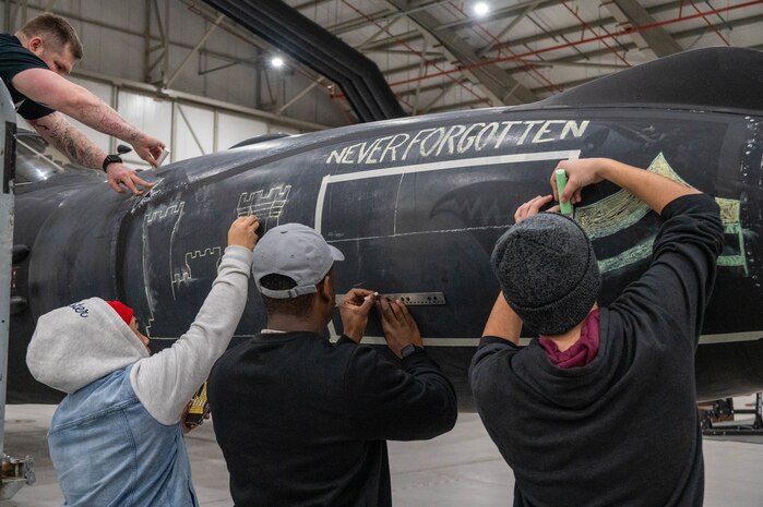 Members of the 99th Expeditionary Reconnaissance Squadron participate in a memorial drawing on a U-2 Dragon Lady.