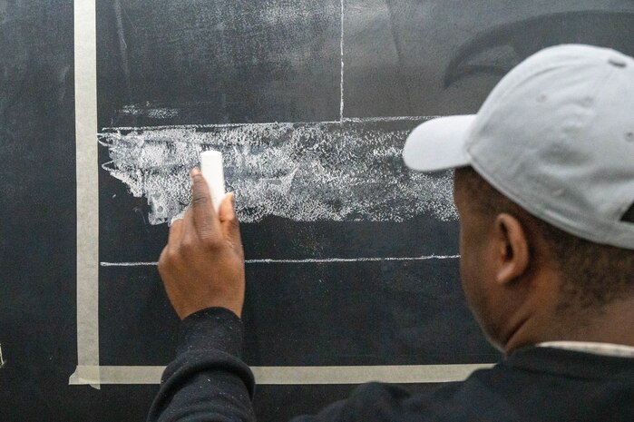 An Airman from the 99th Expeditionary Reconnaissance Squadron sketches out the Georgia state flag as part of a memorial drawing on a U-2 Dragon Lady.