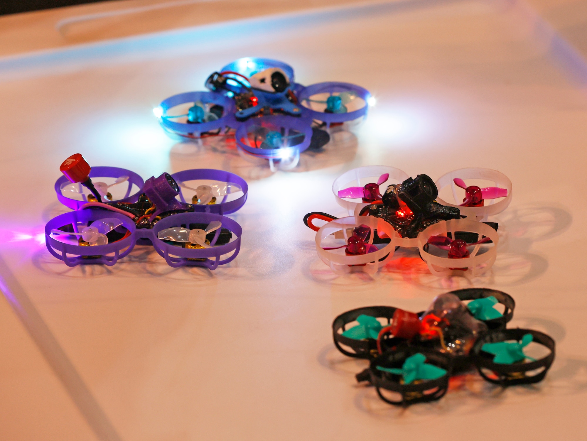 Image of 4 micro drones on a table. One is blue, one is purple, one is red nd the other is green and black. They each have four propellers.