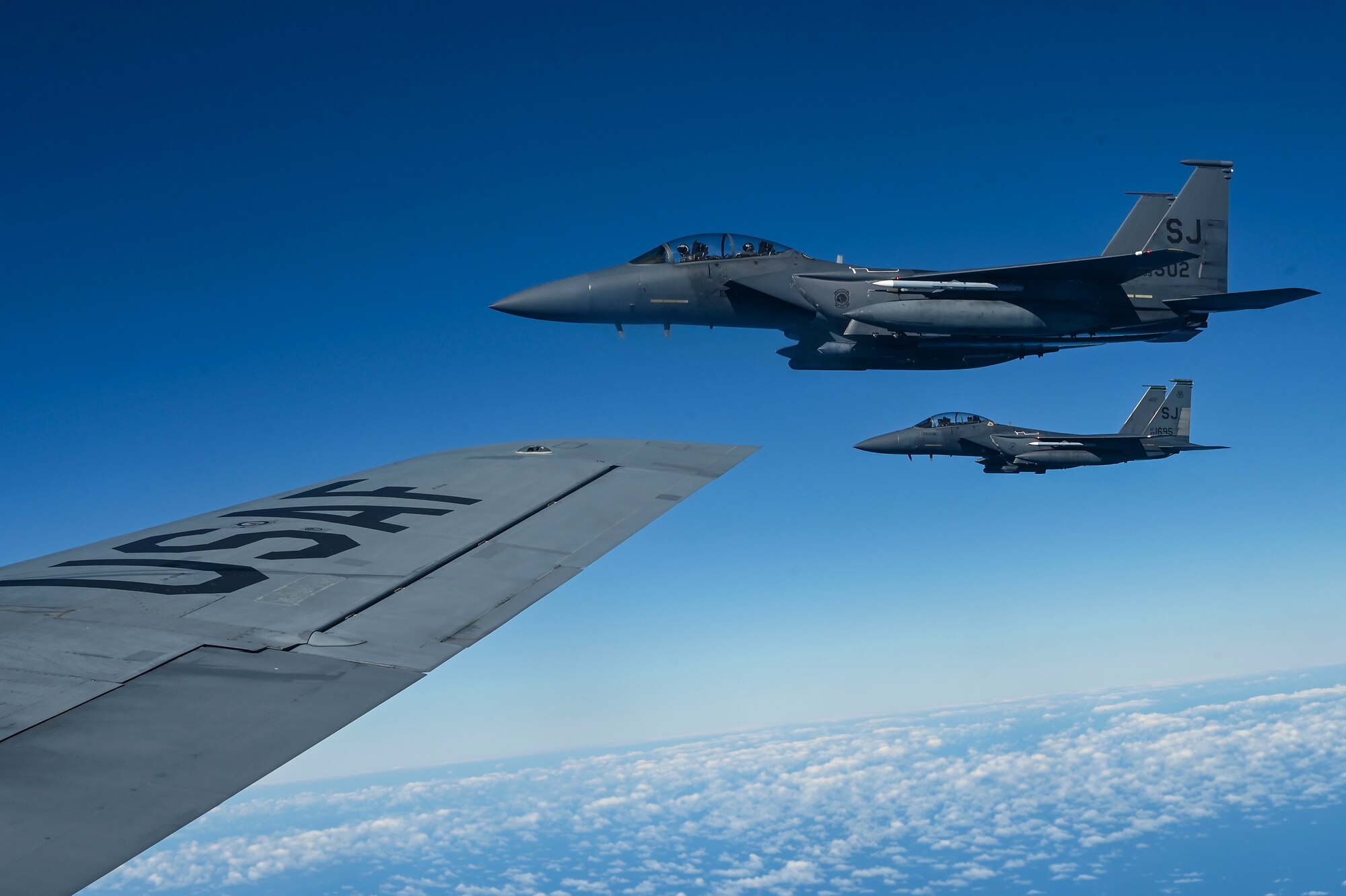Two fighter jets fly beside a KC-135