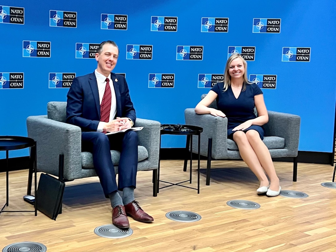 Two researchers siting while posing for photo during a presentation to NATO.